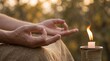 © KBTO - Close up of hands in meditation mudra pose with burning candle outdoors.