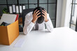 © Charlie's - Asian Businessman Touching Forehead with Headache at Office Desk Experiencing Burnout Stress and Emotional Pain from Boring Job.