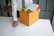 © Charlie's - Businessman Sending Resignation Letter to Boss While Holding Cardboard Box Beside Office Desk After Career Change or Job Loss.