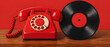 © SIMANG - A vintage red rotary telephone paired with a black vinyl record, placed on a wooden surface against a red backdrop, showcasing retro audio and communication items.