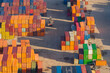 © Amazing Aerial - Aerial view of colorful shipping containers stacked in a large logistics hub with a reach stacker vehicle operating on the ground in Warszawa, Poland.
