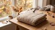 © Sohan212200015 - Folded beige cable knit sweater on a wooden table with autumn decor