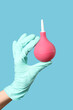 © Pixel-Shot - Medical hygiene and healthcare procedure, hand in latex glove holding a pink rubber enema bulb for clinical treatment on a blue background