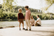 © BGStock72 - Two children enjoy a playful moment by a serene lakeside on a sunny day
