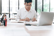 © phaitoon - Professional Male Working at Desk with Laptop and Documents in Modern Office