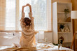 © Pixel-Shot - Morning routine and wellness, woman stretching in bed after waking up in a sunlit bedroom with cozy home interior and soft natural morning light