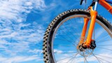 Vibrant Mountain Bike Wheel Against a Bright Blue Sky with Fluffy White Clouds, Perfect for Outdoor Adventure Themes
