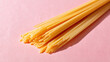 © AnyPic289 - Uncooked spaghetti pasta bundle on pink surface with natural light and shadow