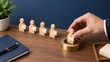 © vatcharapong - goal setting motivation evaluation. Hand placing a wooden figure on a round pedestal with other wooden figures lined up on a desk.