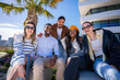 © CarlosBarquero - Multicultural group portrait of friends seated together in a bright residential district with palm trees, modern buildings and warm sunny light.