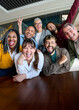 © CarlosBarquero - Vertical. Multicultural coworkers laughing during a lively office meeting, showcasing teamwork, friendship, success, and a vibrant corporate atmosphere.