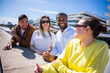 © CarlosBarquero - Multicultural friends enjoy a relaxed social moment while leaning on a ledge in a bright residential area with contemporary buildings.