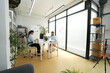 © ultramansk - Two Asian businesswomen in a bright modern office, desk review meeting, desk area with whiteboard sticky notes, medium, soft daylight, successful company culture, Bangkok Thailand