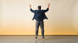 © Strabiliante - Man jumping joyfully in casual attire against beige background