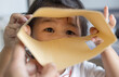 © banjongseal324 - Cute Asian Toddler Girl Peering Through Open Brown Cardboard Sleeve Frame,A close-up lifestyle photograph of a playful cute young Asian toddler girl peering through an open brown paper envelope.