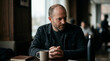 © Vasilii - Pensive mature man with a beard sits at a wooden table in a cafe next to a cup of coffee and a notepad
