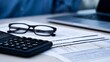 © Bussakon - A close up view of a calculator  eyeglasses  and financial documents on a desk with a laptop in the background