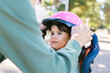 © Evgeniia Primavera - Young girl wearing pink star helmet while parent adjusts chin strap outdoors, closeup family safety moment, child cycling preparation, sunny park, protective gear, active lifestyle concept