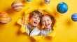 © ZaStock - Cheerful children peering through a hole in yellow paper surrounded by floating planets, cosmic theme. Space exploration, education, imagination, childhood fun.