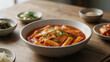 © phumin - An inviting close-up of a vibrant bowl of traditional Korean spicy rice cakes, Tteokbokki, beautifully garnished, surrounded by fresh, assorted banchan on a rustic wooden table