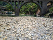 © Graphixa - Ancient stone bridge arches gracefully over a dried riverbed filled with smooth pebbles during a bright summer day in a lush and verdant natural landscape
