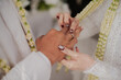 © MUSTAGFIRIN - romantic moment of a bride placing a wedding ring onto the groom's finger during a traditional Indonesian wedding ceremony.