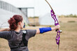 © Cavan Images - Young woman practicing archery with a purple bow