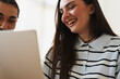 © Studio Marmellata - A young man and woman look at a laptop computer together. They are smiling and laughing while watching something funny on the screen in a bright indoor room.