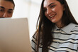 © Studio Marmellata - A young man and woman look at a laptop screen together. They are smiling while browsing content on the computer, sharing a pleasant moment in a bright indoor setting.
