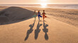 © Rendara Studio - Three multicultural friends in tree pose cast long shadows across the dune