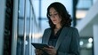 © Prapan - Businesswoman Working with Tablet in Modern Office: A focused businesswoman in a sharp suit navigates a tablet, surrounded by the sleek, contemporary architecture of a modern office building.