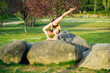 © Metadancer - White woman performing flexible yoga pose outdoors on rock in park