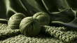 © Audrey - Soft, green wool yarn balls sit atop a textured crochet blanket. Dark, smooth satin drapes hang behind, enhancing a luxurious yet contrasting ambiance. Natural fibers gather in a cozy setting, primed