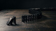 © MR Crafts - Domino effect photo showing black dominoes falling on a wooden table in a chain reaction concept business strategy risk line impact success failure consequence trigger management planning challenge