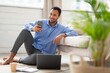 © Prostock-studio - Happy Male, Young Adult, Black, Sitting On Floor With Laptop And Smartphone At Home, Engaged In Work Or Communication. Comfortable Setting Indicating Remote Work Lifestyle, Business Concept.