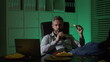 © Volodymyr - Businessman eats a late-night snack while working on laptop. A tired employee using laptop on late-night overtime. Business man overworked into the night. Freelancer eat pizza late at night.