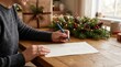 © Matweymax - Person writing a handwritten holiday card or gift list at a wooden table beside festive evergreen decor, wrapped present and warm window light in a cozy home interior for advertising and editorial des