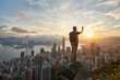 © Asia Pics - Mature man using phone, taking photo of city view of Hong Kong skyline, from Victoria peak at sunrise