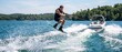 © ProNoJoy - A man wakeboarding on a blue lake, jumping into the air while being towed by a white motorboat, with a forested shoreline in the background, under a clear sky