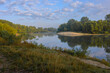© Александр Арендарь - A scenic, peaceful river flows gently under a partly cloudy blue sky, its calm surface perfectly reflecting the lush green forests and sandy banks lining both sides during a bright morning.