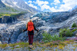 © M.studio - Female hiker with red backpack and poles standing in front of impressive alpine glacier ice in French Alps