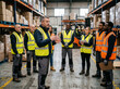 © NikonLamp - Warehouse supervisor briefing diverse logistics team among stacked boxes and forklift on gray background.
