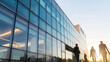 © Fahroni - The exterior of a sleek, modern office building on a sunny day, with reflective glass windows and pedestrians walking by, highlighting the dynamic flow of corporate life in an urban business district.