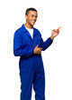 © geng - Young Smiling African American Mechanic in Blue Overalls Pointing to the Side Isolated on White Background