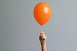 © Studio Nova - The Orange Balloon Held Aloft by a Human Hand in a Minimal Studio Portrait