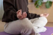 © Wavebreak Media - Female in brown top, beige sweatpants meditating on purple yoga mat at home near wooden cabinet