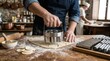 © wahid - Professional baker using metal cutter for raw dough in rustic kitchen