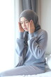 © unikyluckk - Young Muslim woman suffering from severe headache at home. Asian woman wearing hijab touching her painful temples on bed. Hijabi girl feeling discomfort and migraine symptoms in bedroom.