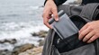 © krismicrostoker - Hand inserting sealed case into backpack near ocean waves