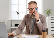 © Pixel-Shot - Bearded businessman with laptop talking by mobile phone at desk in office